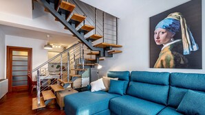 A modern living room with a blue sofa, a staircase with wooden steps, and a large painting on the wall. - Giano Della Bella (Florence)