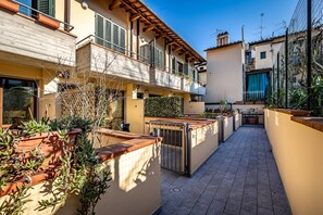 A narrow outdoor corridor with potted plants, a metal gate, and a tiled floor. - Giano Della Bella (Florence)