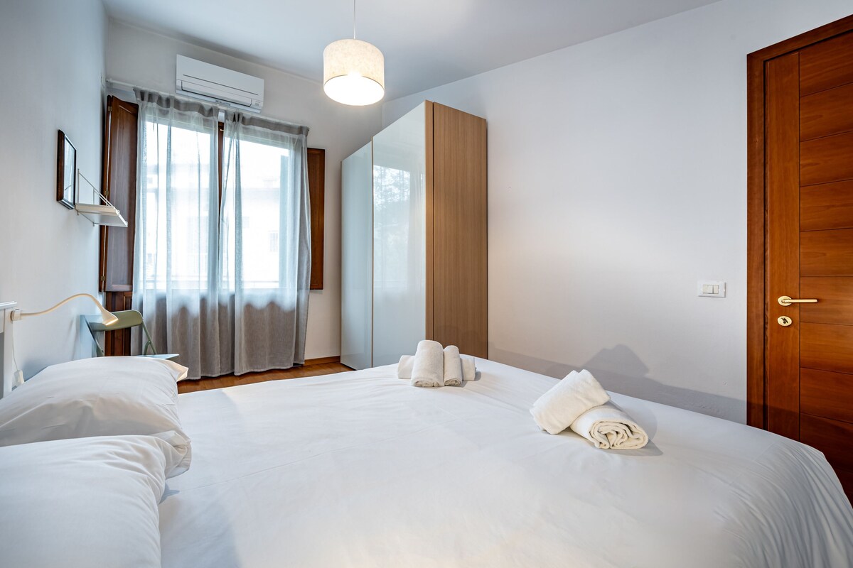 Een hotelkamer met een groot bed, een kledingkast, een spiegel en een raam met gordijnen.