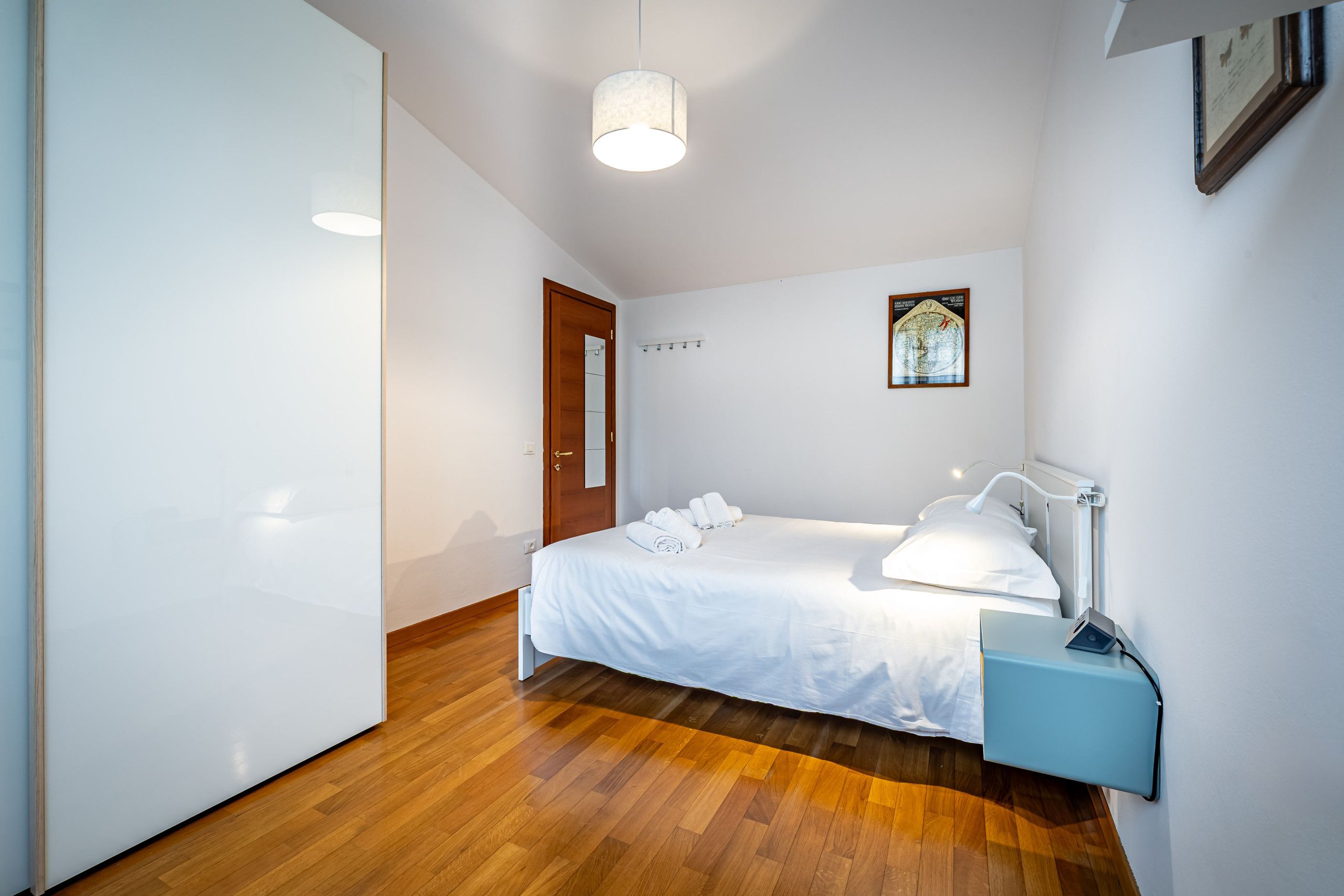 Une chambre d’hôtel avec un lit, une table de chevet, une lampe, une carte accrochée au mur et un plancher en bois.