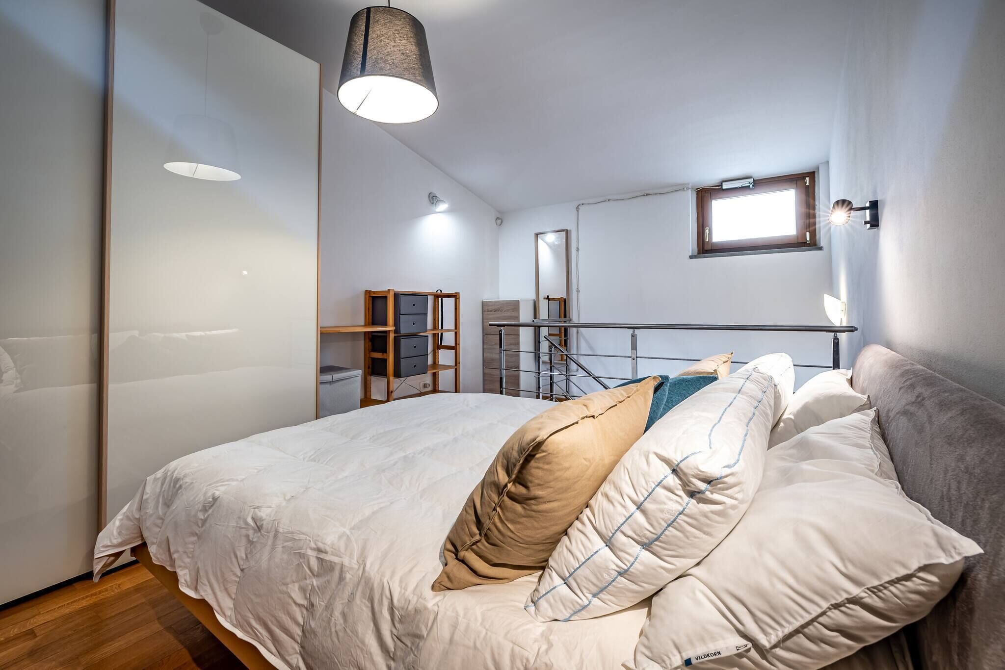 A modern bedroom with a large bed, a wooden ladder, a small window, and a mirror on the wall.