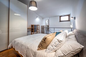 A modern bedroom with a large bed, a wooden ladder, a small window, and a mirror on the wall. - Giano Della Bella (Florence)