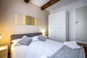 Ein ordentlich bezogenes Bett mit Kissen, einer Nachttischlampe und einem großen Kleiderschrank im Hotelzimmer.