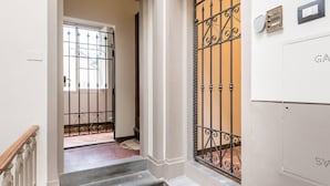 Escada que leva a uma porta com portão de ferro forjado, interruptor de luz e termostato na parede.