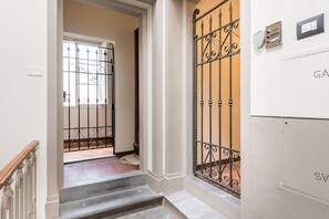 Eine Treppe führt zu einer Tür mit schmiedeeisernem Gitter. An der Wand befinden sich ein Lichtschalter und ein Thermostat.