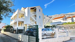 Un edificio a più piani con facciata bianca, una scala visibile e un’area parcheggio recintata.