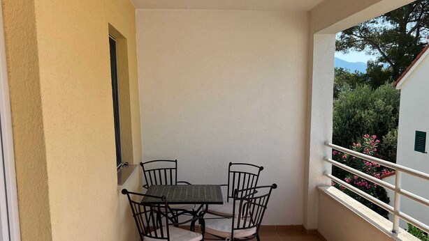 Un piccolo balcone con tavolo e sedie, una finestra e vista su piante.