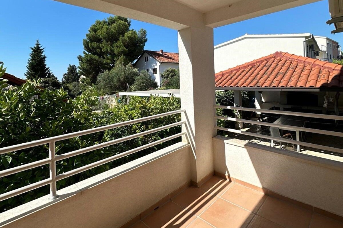 Ein Balkon mit Fliesenboden und weißem Geländer, der auf einen Wohnbereich mit Häusern und Grünflächen blickt.