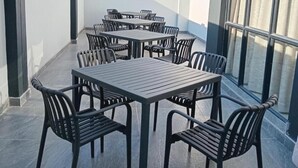 Eine Terrasse mit mehreren Tischen und Stühlen, einem Fliesenboden und Blick durch große Fenster.