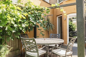 Une terrasse avec une table ronde et des chaises, une clôture en bois et un pot de fleurs.