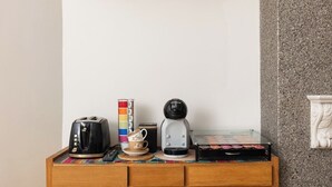Ett litet träbord med en kaffebryggare, en brödrost, en mugg och en ask te.