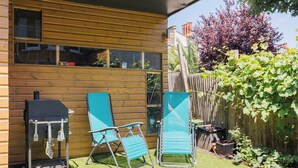 Ett trähus med en grill, två blå trädgårdsstolar och ett trästaket.