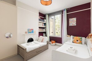 Une chambre avec une cheminée, une bibliothèque, une fenêtre avec des rideaux et un lit agrémenté d’un coussin coloré.