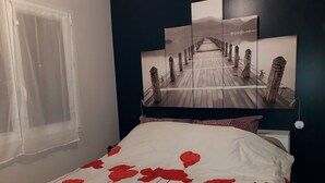 A bedroom with a bed, a window with curtains, and a wall with a framed picture. - A charming 32 m² studio apartment with an adjoining terrace. (Les Pennes-Mirabeau)