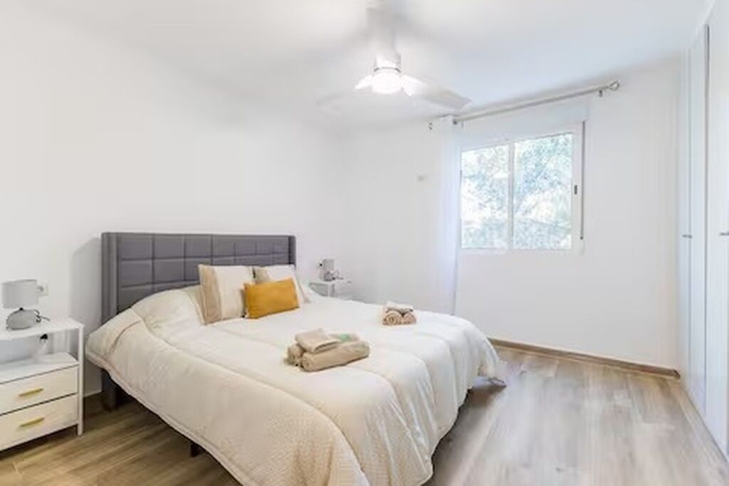 A bedroom with a bed, bedside tables, a ceiling fan, and a window.