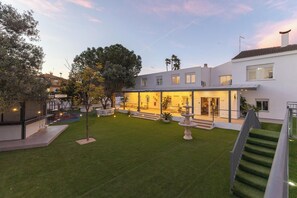 Een modern huis met twee verdiepingen, een verzorgd gazon, een terras en een fontein.