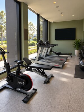 Un gimnasio con máquinas de cardio, bancos de pesas y un amplio ventanal con vistas al exterior.