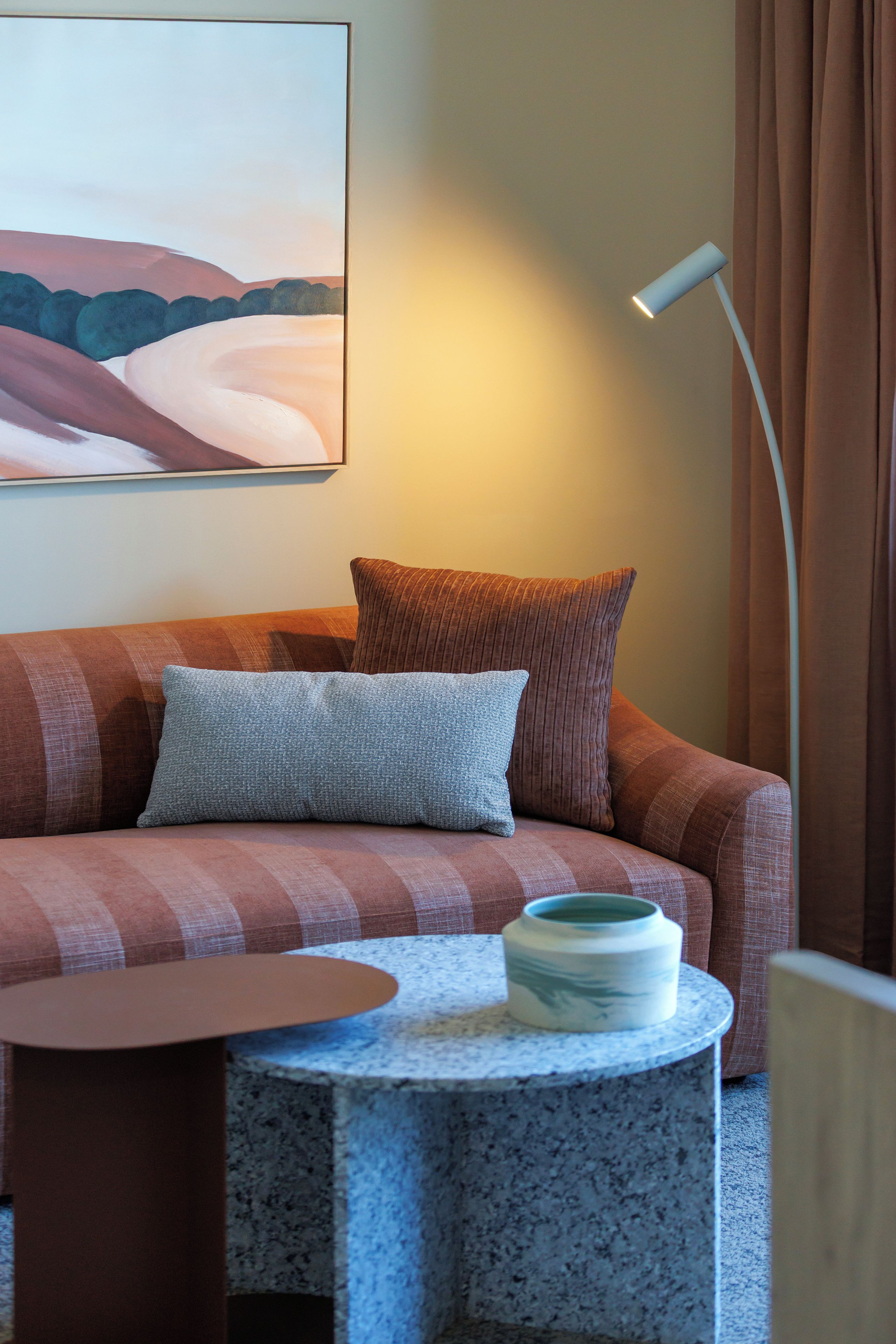Een moderne woonkamer met een bank, een rond bijzettafeltje, een vloerlamp en een schilderij aan de muur.