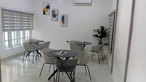 Een moderne vergaderzaal met een marmeren vloer, ronde tafels en stoelen, een airconditioning en kunstwerken in lijsten aan de muur.