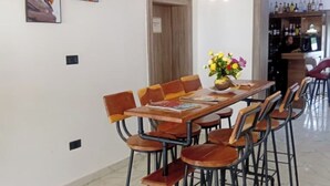 Een eetgedeelte met een houten tafel en stoelen, een vaas met bloemen, en een bar met flessen op de planken.
