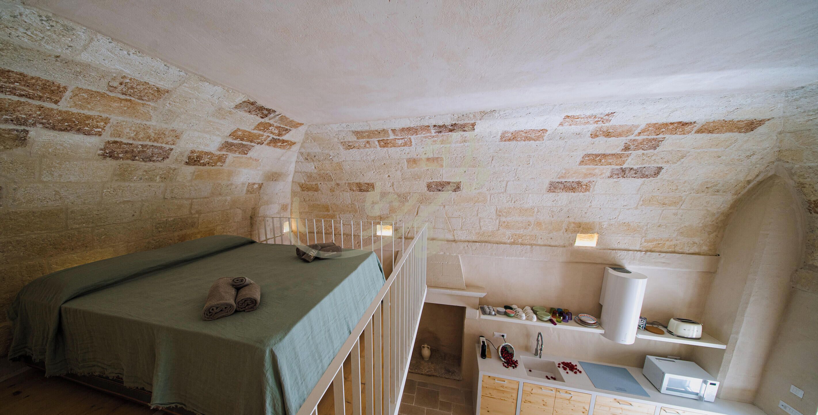 A room with a bed, a small kitchenette, and a brick wall.