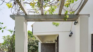 Eine überdachte Terrasse mit Tisch und Stühlen, einer Pergola und Blick in einen Raum mit Fliesenwand.