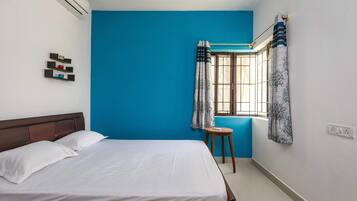 A room with a bed, a stool, a window with curtains, and an air conditioning unit.