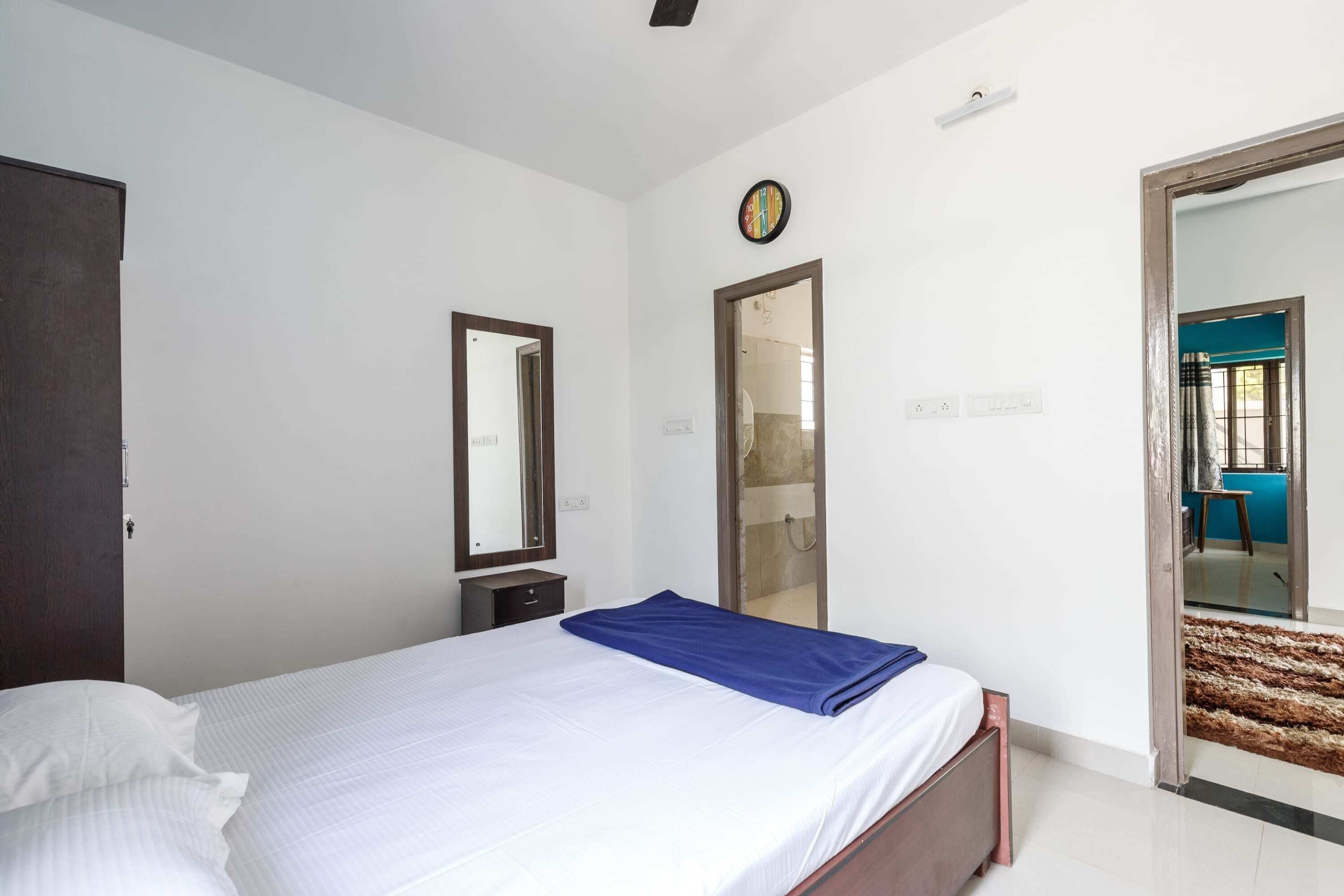 A bedroom with a bed, a mirror, a door, and a view into another room.