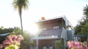 Ein modernes, zweistöckiges Haus mit Balkon, umgeben von viel Grün und einem kleinen Pool.