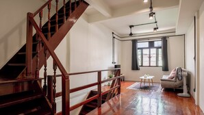 A spacious room with a wooden staircase, a large window with curtains, a fan, and a small table with a plant. - Cool Cozy 3-bedroom townhome in Chinatown Krung Thep Maha Nakhon (Krung Thep Maha Nakhon)