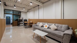 A modern living room with a grey sofa, white coffee table, wooden paneling, and a dining area with chairs and a table. - Cool Cozy 3-bedroom townhome in Chinatown Krung Thep Maha Nakhon (Krung Thep Maha Nakhon)