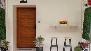 A building entrance with a wooden door, potted plants, two stools, and a small shelf with flowers. - Cool Cozy 3-bedroom townhome in Chinatown Krung Thep Maha Nakhon (Krung Thep Maha Nakhon)