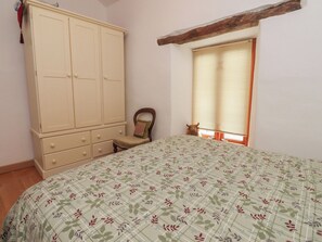 A bedroom with a bed, a wardrobe, a chair, and a window with blinds. - The Cottage (Settle)