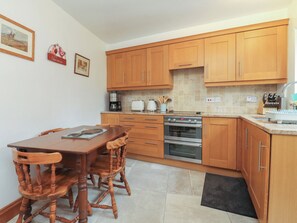 A kitchen with wooden cabinets, a dining table with chairs, a coffee maker, a toaster, and an oven. - The Cottage (Settle)