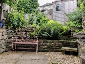 A garden with a metal bench, stone wall, and a wooden fence. - The Cottage (Settle)