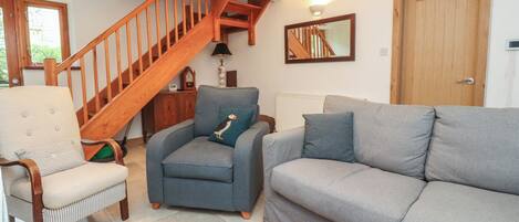 A living room with a wooden staircase, a grey sofa, a blue armchair, and a wooden coffee table with a magazine.