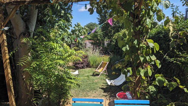 Un patio in legno con una panchina, un'amaca e un'area giardino con diverse piante.