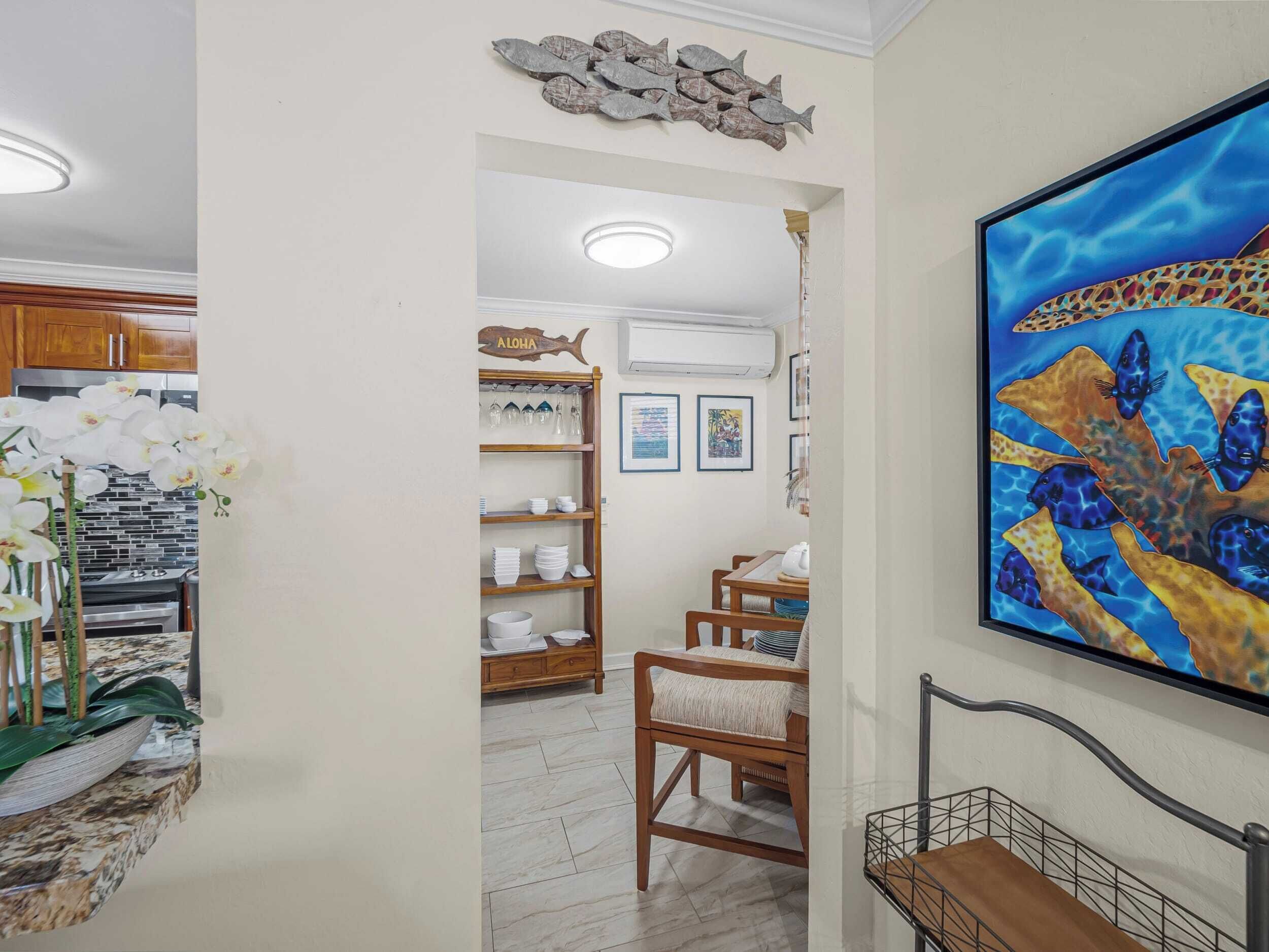 A hallway with a kitchen area, a dining table with chairs, a bookshelf, and a framed painting.