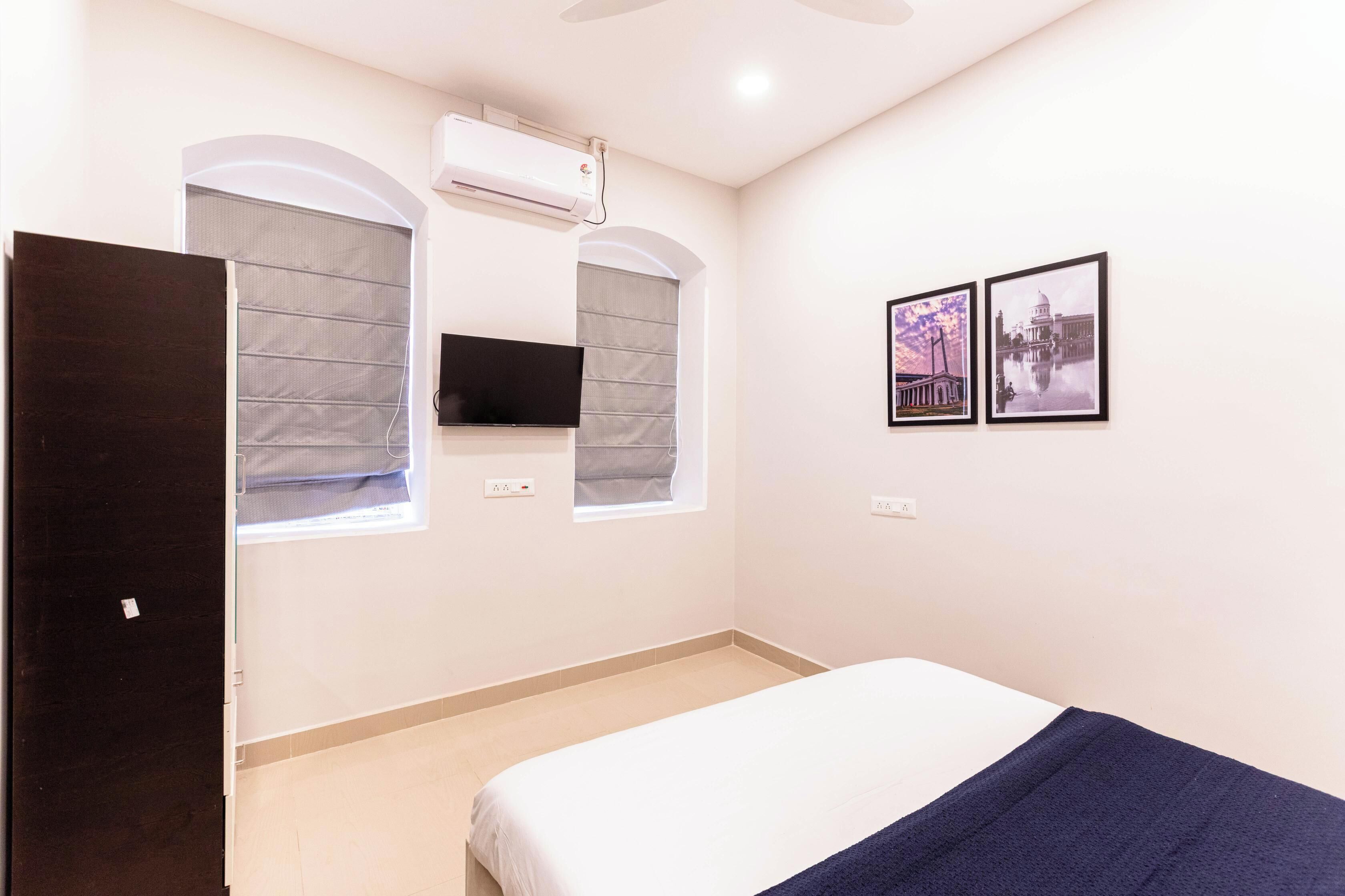 A bedroom with a bed, a TV mounted on the wall, and two framed pictures.