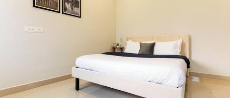 Un dormitorio ordenado con una cama, una mesita de noche y dos cuadros enmarcados en la pared.