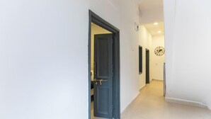 A hallway with a dark door, white walls, and a clock on the wall.