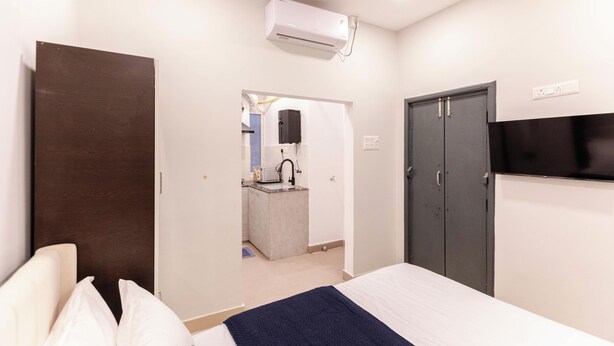 A hotel room with a bed, a TV, a wardrobe, and a kitchenette.