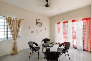 A room with a dining table, four chairs, a ceiling fan, and a window with curtains. - Azure Lumina by Stayjade3bhkpool Garden1hr HSR (Shoolagiri)