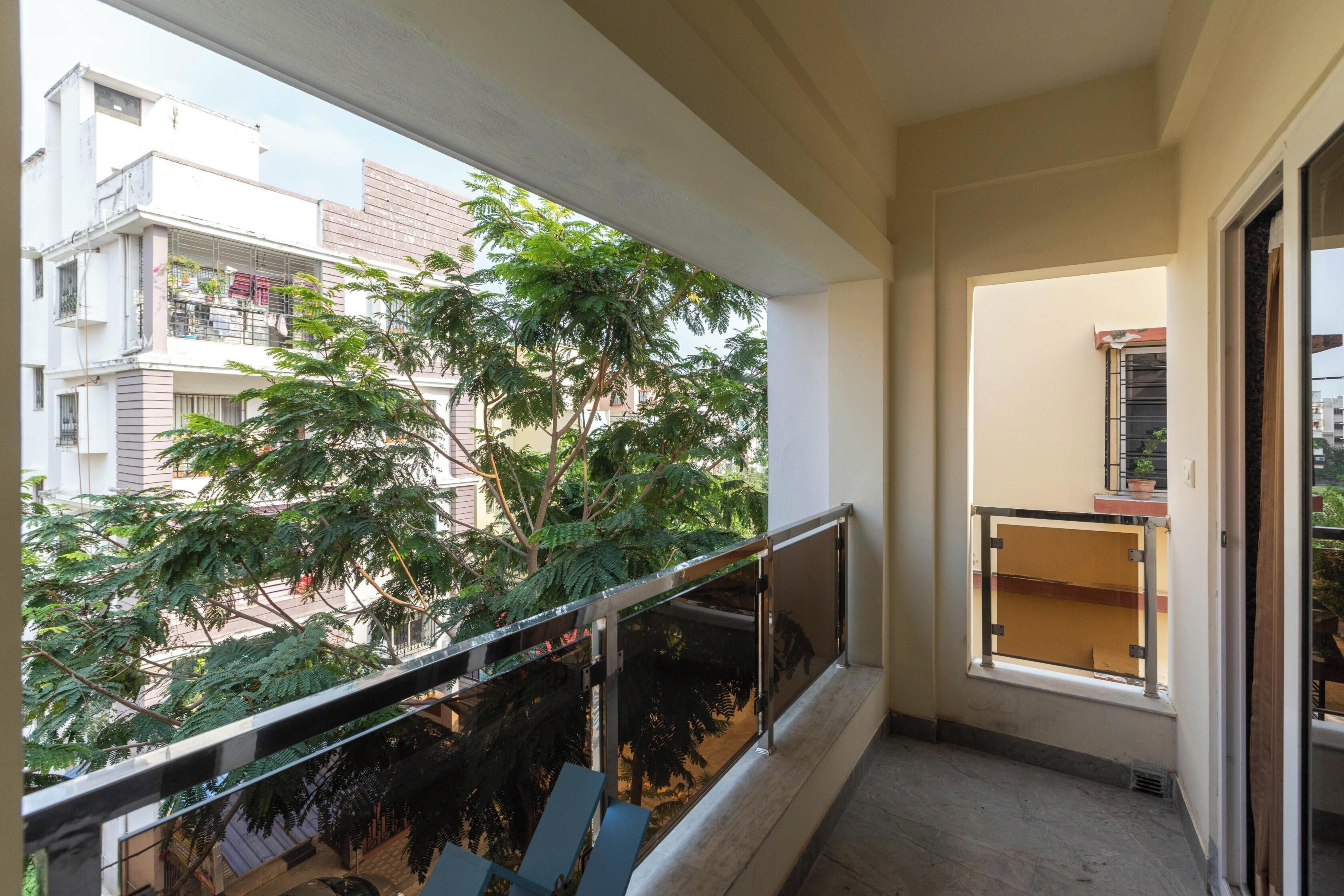 Een balkon met een glazen hekwerk, uitzicht op omliggende gebouwen en een boom.