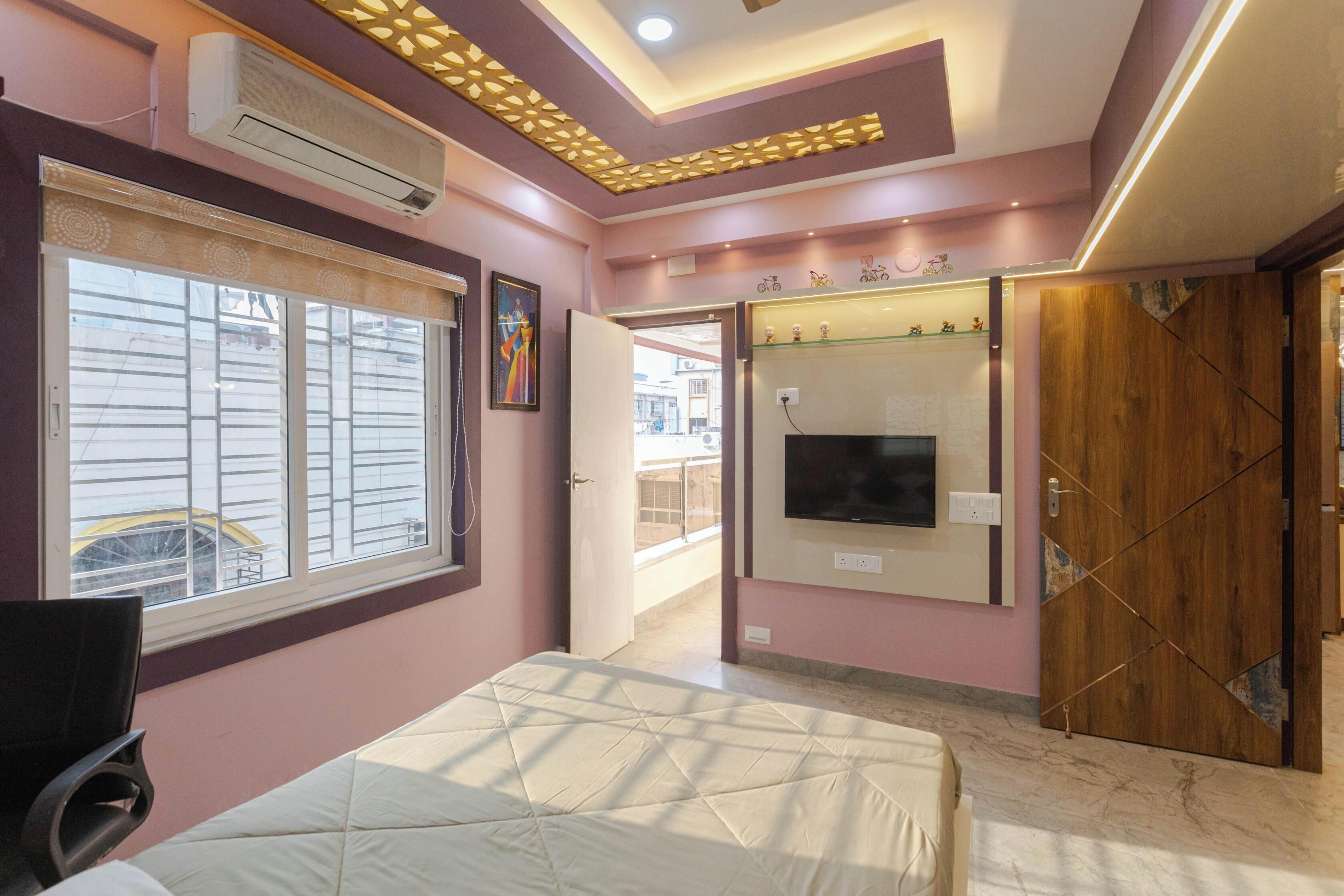 A bedroom with a bed, a TV, a wardrobe, and a window with blinds.