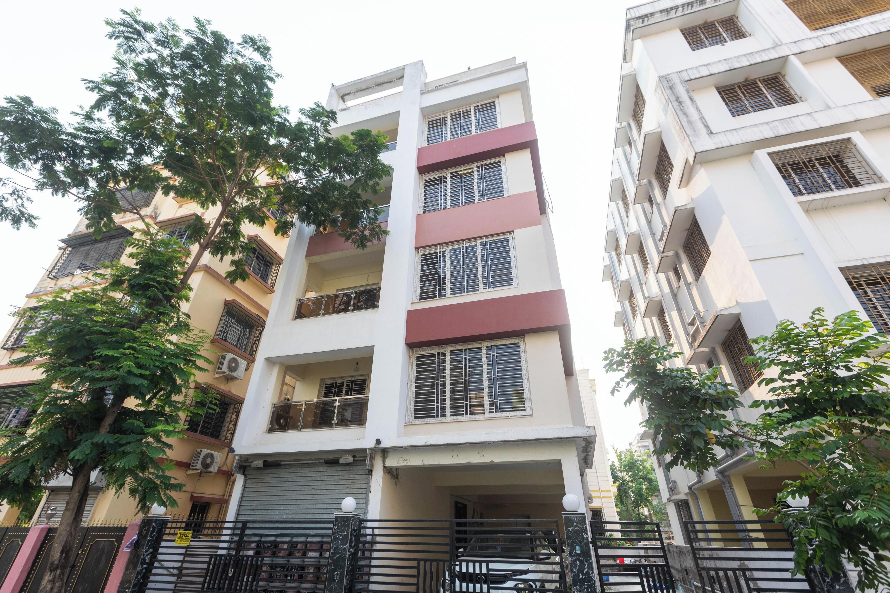 A multi-story residential building with balconies, a gated entrance, and trees in the foreground.