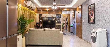 A modern living room with a sofa, TV, ceiling fan, and air conditioning unit.