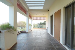 A covered corridor with a tiled floor, a glass door, and a view of greenery outside. - Aurora Mansion by Red Olive 3bhk Nr ECR Beach (Chennai)