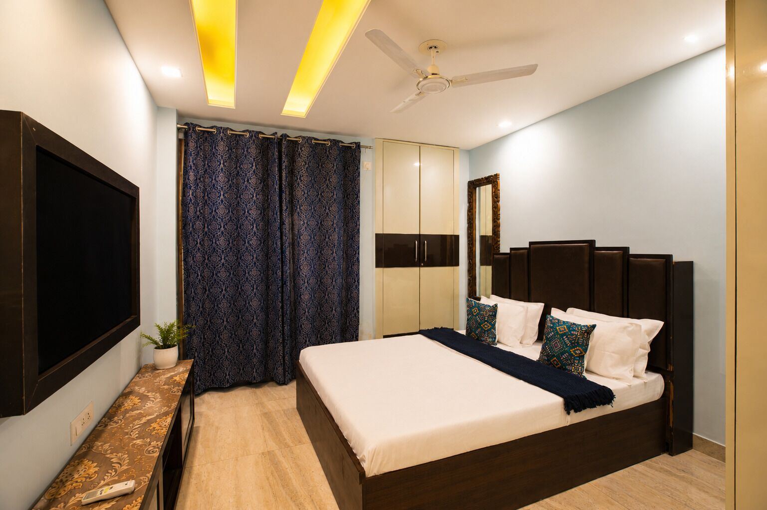 A modern bedroom with a large bed, a TV, a ceiling fan, and a wardrobe.