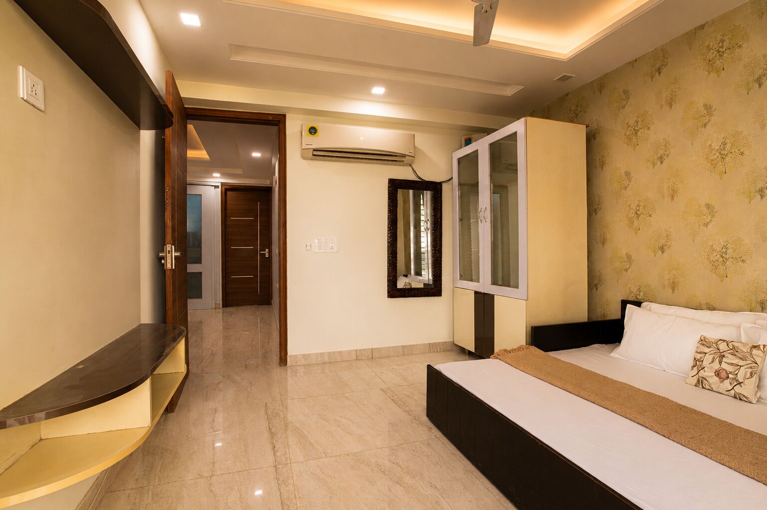 Une chambre d’hôtel comprenant un lit, une armoire, un miroir, un appareil de climatisation et une porte donnant sur une autre pièce.